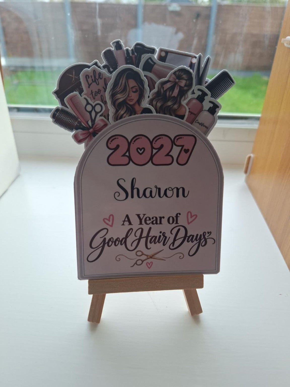 Personalised 2027 hairdresser desk calendar on its wooden stand; Sharon is an example name